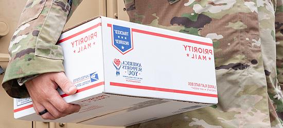 Military service member holding Priority Mail box.